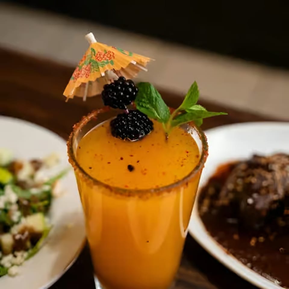 Mexican drink with a sugar-rimmed glass, garnished with blackberries, mint, and a paper umbrella.