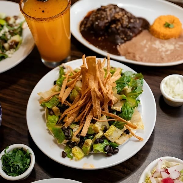 Mexican salad with black beans, avocado, and tortilla strips, with other dishes and a drink.