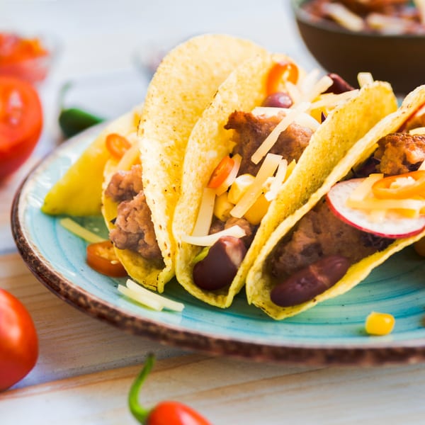 Three El Jacal Mexican Grill tacos with meat, cheese, beans, and vegetables on a blue plate.