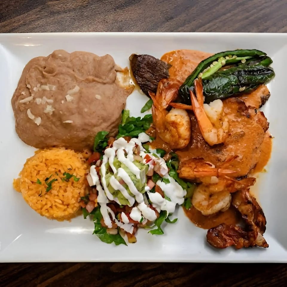 Mexican dish with shrimp, steak, grilled peppers, refried beans, rice, and a salad with dressing.