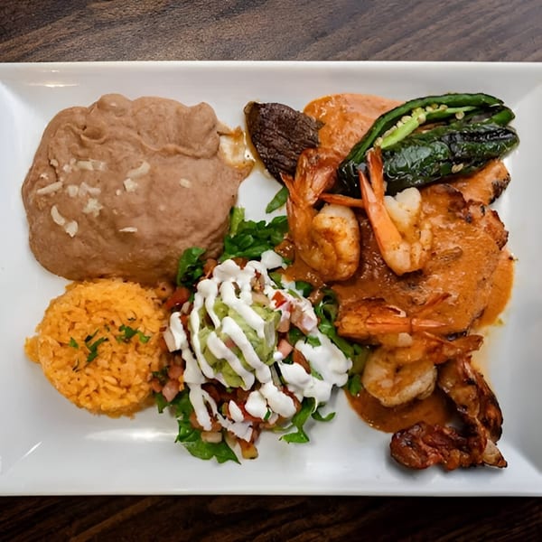 Mexican dish with shrimp in red sauce, refried beans, rice, and a side salad with guacamole.