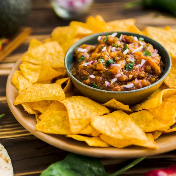 A bowl of El Jacal Mexican Grill's salsa with red onions and cilantro, surrounded by tortilla chips.